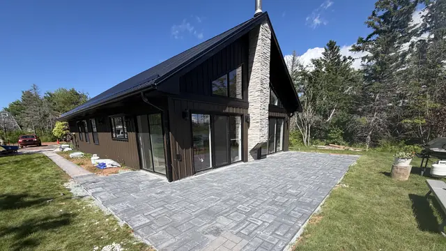 Large charcoal paver patio in a basket-weave pattern beside a black modern chalet