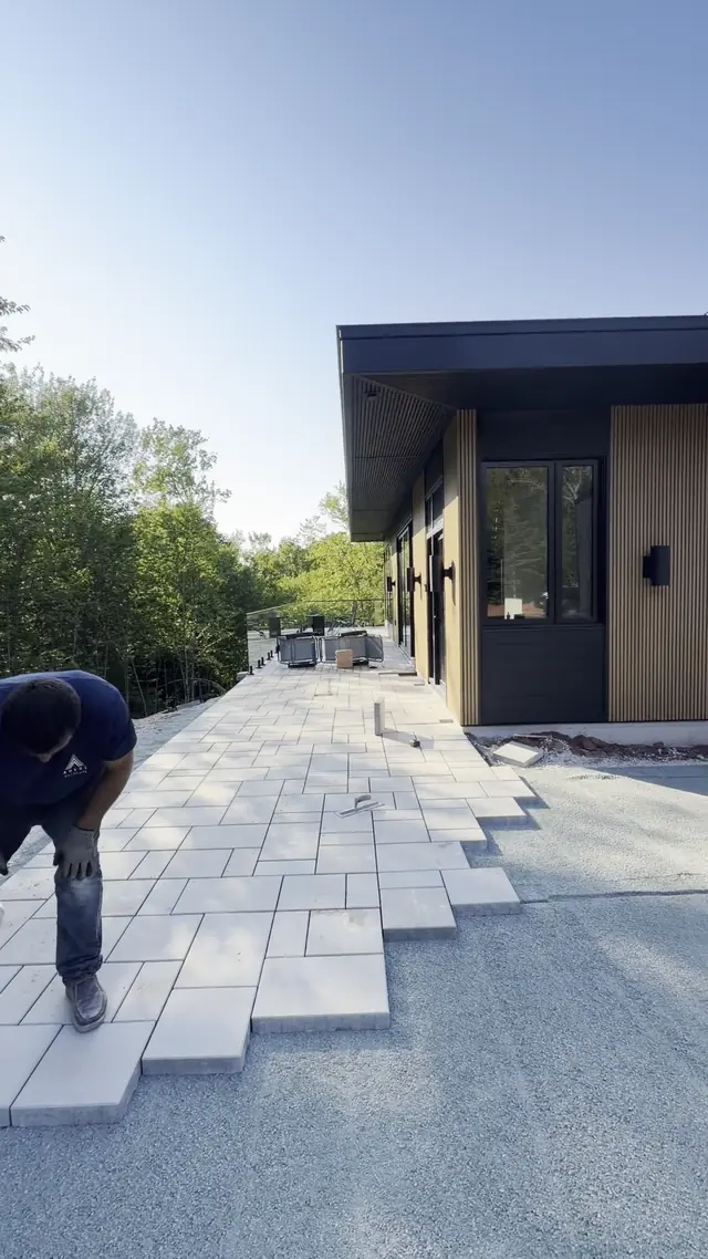 Crew laying large-format light slabs on a screeded base along a modern home