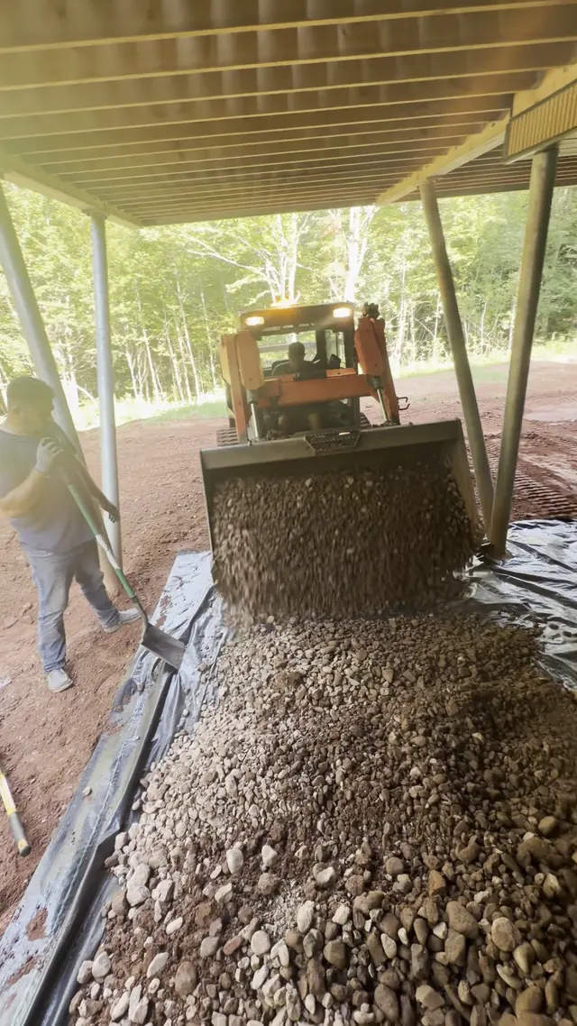 Track loader dumping clear stone under a raised deck while the crew spreads it over landscape fabric