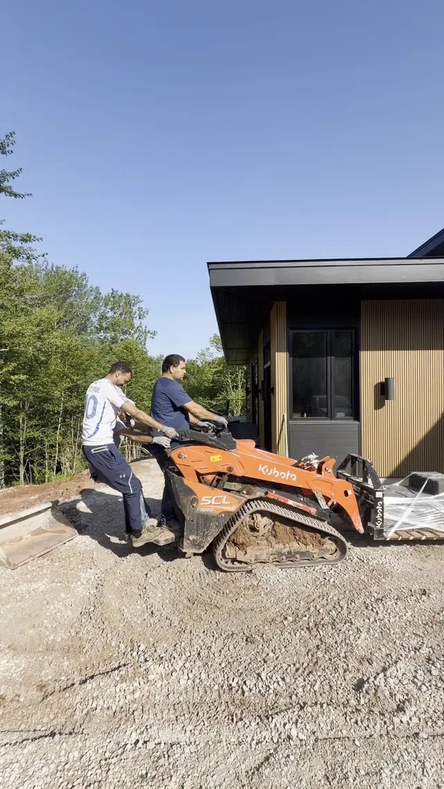 Aderz crew spreading a gravel base with the Kubota SCL1000 track loader beside a modern cedar-clad home