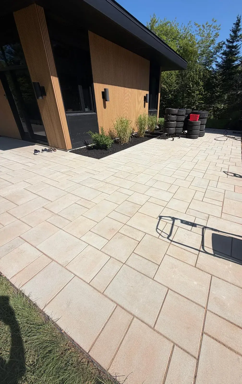 Large-format light slab patio wrapping a modern cedar-clad home, with a mulch bed and ornamental grasses