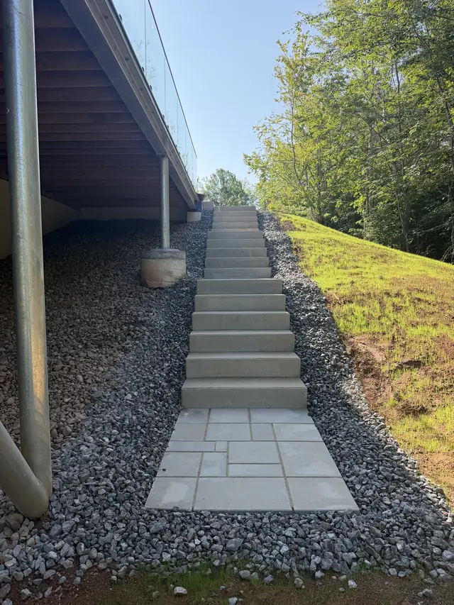 Slab steps climbing a slope under a glass-rail deck, edged with river stone